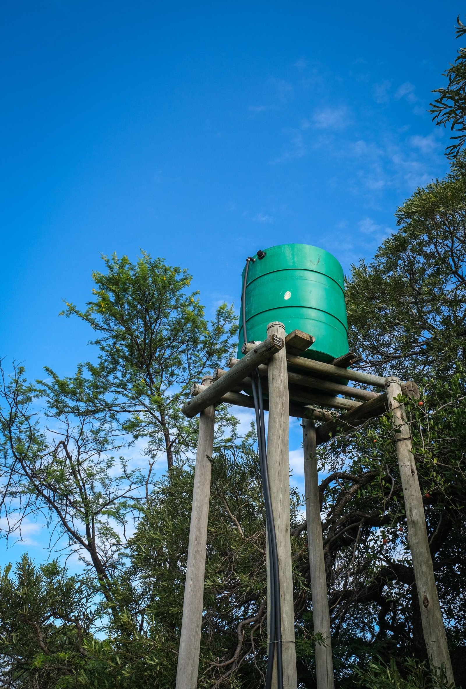 A photo of an elevated green water tank supported by a wooden frame, set against a clear blue sky.
